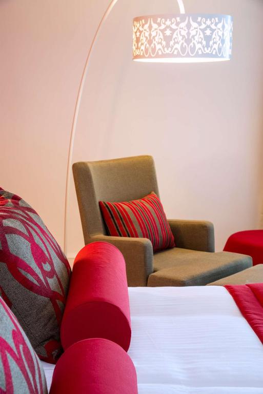 Mūsdienīgi iekārtota guļamistaba ar sarkaniem akcentiem, ērtiem krēsliem un stilīgu lampu, radot siltu un viesmīlīgu atmosfēru.