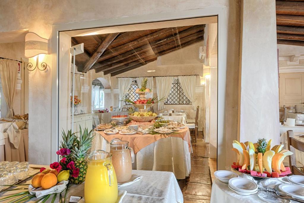 Elegants restorāna interjers ar bagātīgu brokastu bufeti, kurā redzami dažādi augļi, dzērieni un uzkodas. Gaismas apgaismojums un koka griesti piešķir siltu atmosfēru.