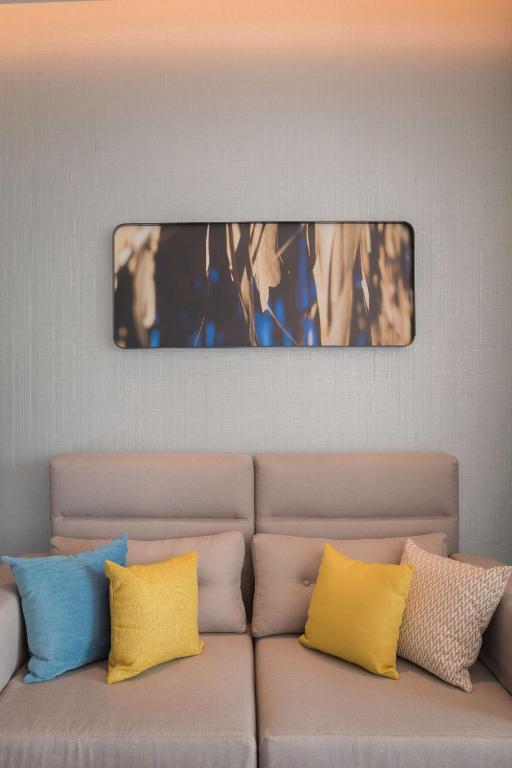 Mūsdienīgs viesistabas interjers ar pelēku dīvānu un spilveniem dzeltenā un zilā krāsā, kā arī mākslinieciskais attēls uz sienas.