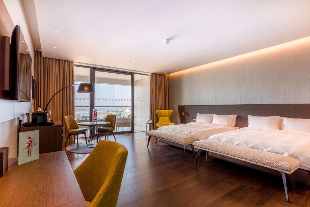 Mūsdienīgs viesnīcas numurs ar divām gultām, ērtu dīvānu un skatu uz ārpusi. Telpā ir moderna mēbeļu kompozīcija un lieli logi, kas nodrošina dabisko apgaismojumu.