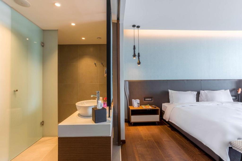 Mūsdienīga viesnīcas istaba ar stikla dušu un elegantu vannu, kas atrodas blakus guļamistabai ar mīksto gultu un stilīgu apgaismojumu.