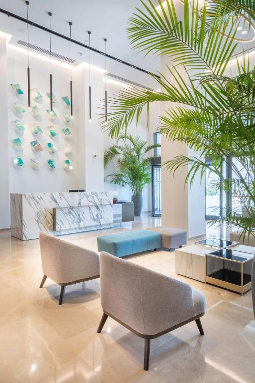 Mūsdienīgs reģistratūras interjers ar marmora letēm, greznām mēbelēm un zaļām palmu lapām, kas piešķir telpai svaigumu. Eleganti gaismas elementi un mākslinieciskas detaļas veido patīkamu atmosfēru.