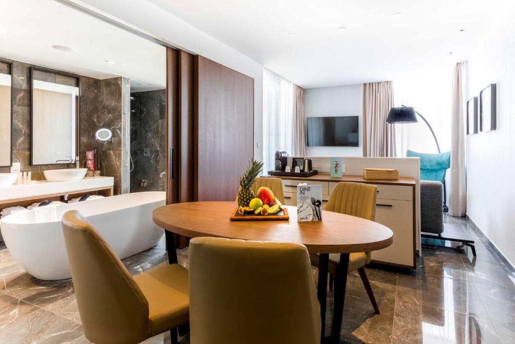 Mūsdienīgs viesnīcas numurs ar viesistabu, ēdamgaldu un atpūtas zonu, kurā redzama moderna vannas istaba. Interjers ar greznām detaļām un dabīgiem toņiem.