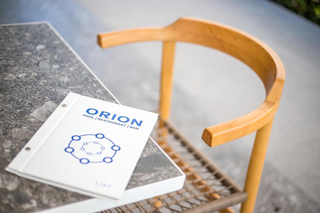 Restorāna "ORION" ēdienkarte atpūtas zonā uz akmens galda, blakus koka krēslam.