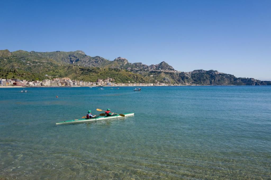 Kajaks diviem cilvēkiem mierīgā jūrā ar kalnu ainavu un krastmalu fona. Skaidrs debesis un saulains laiks.