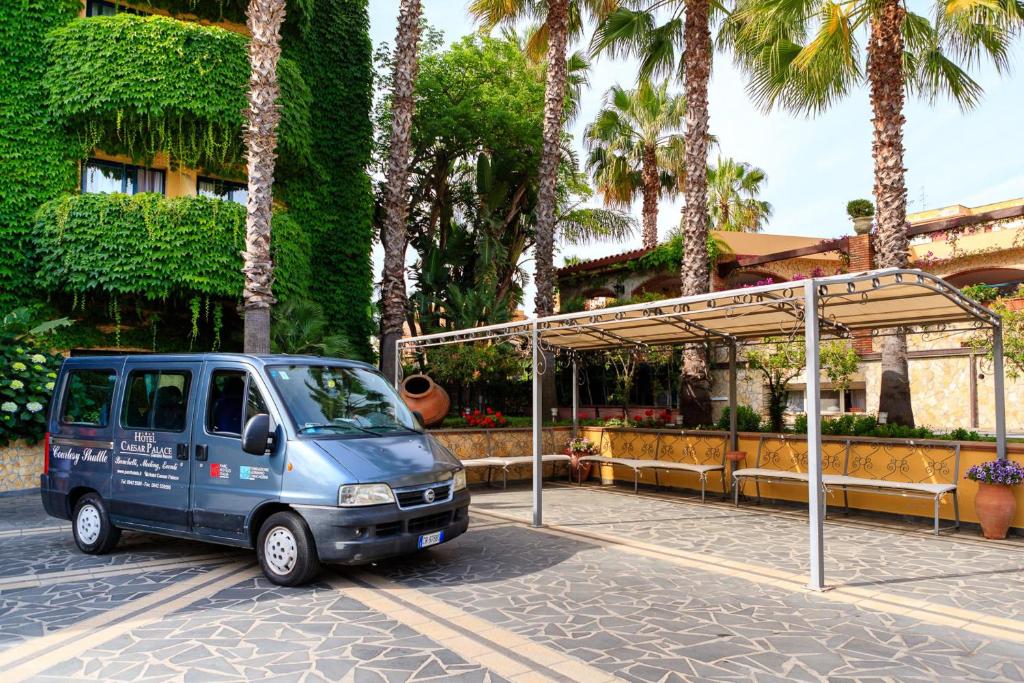 Autobuss stāv pie viesnīcas Caesar Place, ko ieskauj zaļumi un palmas. Apkārt ir sakopta teritorija ar sēdvietām un dekoratīviem augiem.