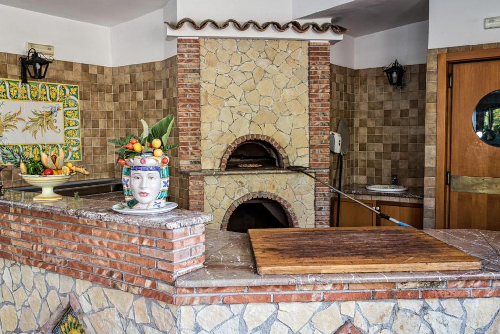 Virtuves zona ar akmens krāsni, dekoratīvu trauku ar augļiem un flīzēm, kas piešķir vietai mājīgu atmosfēru.