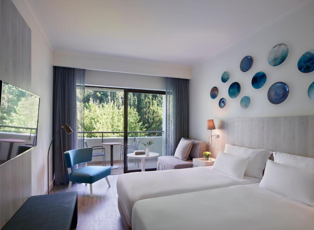 Mūsdienīga viesnīcas numura interjers ar divām atsevišķām gultām, televizoru un piekļuvi balkonam. Sienas rotā krāsaini mākslas darbi, radot relaksējošu atmosfēru.