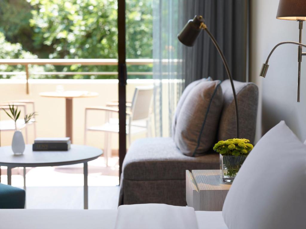 Mūsdienīgs viesnīcas numurs ar ērtu dīvānu, galdu un zaļiem augiem, kas sniedz patīkamu atmosfēru. Gaismas pieplūdums caur logiem radīšanai harmonisku vidi.