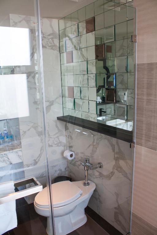 Mūsdienīga vannas istaba ar stikla sienu, kas atspoguļo elegantu mozaīkveida spoguli un marmora apdari. Tajā ir tualete un melna darba virsma.