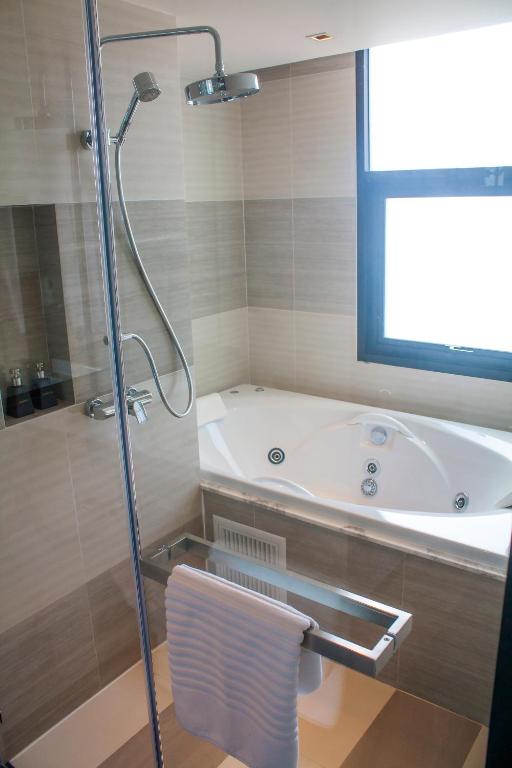 Mūsdienīga vannas istaba ar dušu un burbuļvannu, logu, kas nodrošina dabīgu apgaismojumu, un glītu dvieļu turētāju.