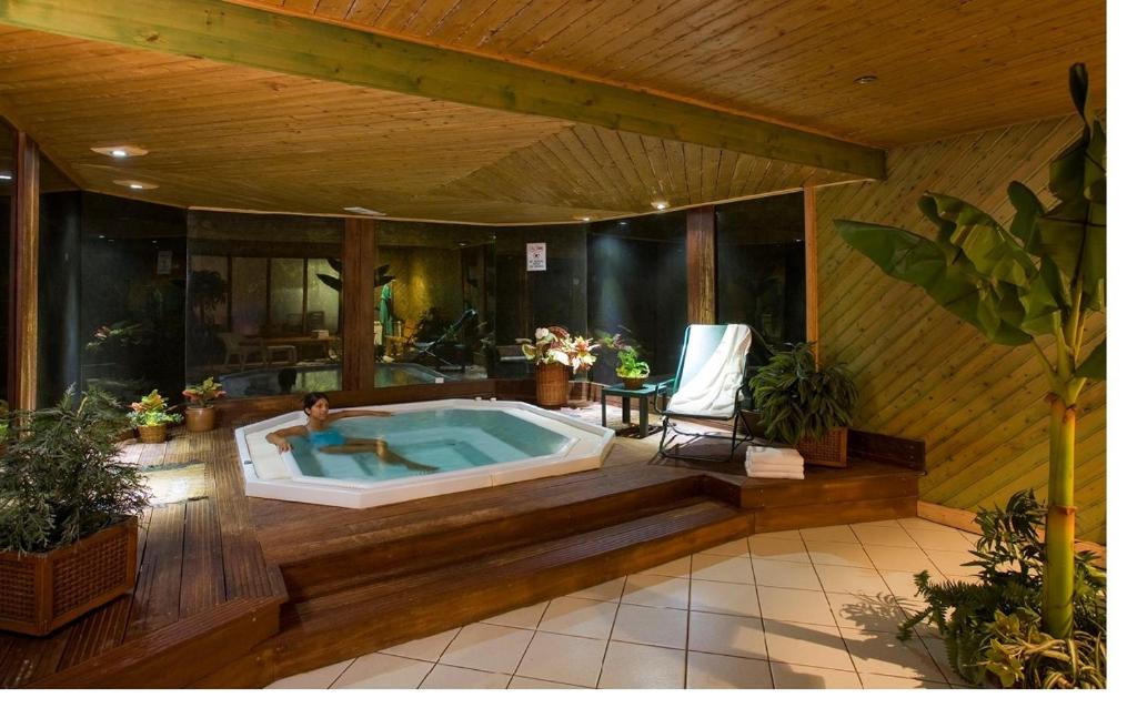 Relaksējoša spa telpa ar džakuzi, kurā atpūšas cilvēks, apņemts ar zaļām augu kompozīcijām un modernu interjeru. Ideāla vieta relaksācijai un atjaunošanai.