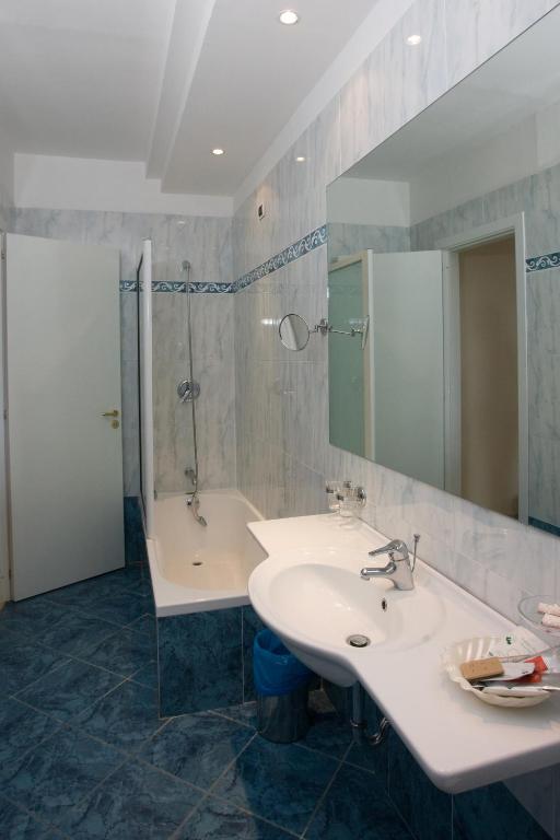 Mūsdienīgs vannas istabas interjers ar vannu, dušas stūri un divu izlietņu izkārtojumu, ko papildina gaišas flīzes un spoguļi.