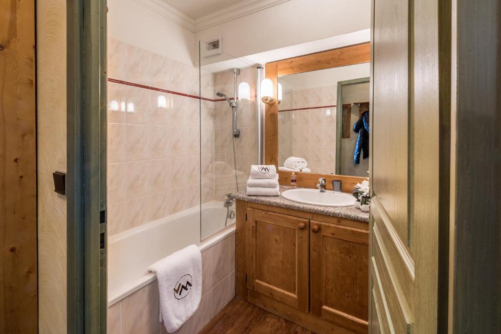 Mūsdienīga vannas istaba ar koka elementiem, vannu un dušas kabīni, papildināta ar elegantu spoguli un higiēnas piederumiem.