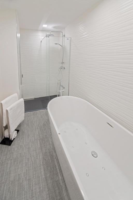 Mūsdienīga vannas istaba ar elegantu brīvo stūra vannu un stikla dušu, apvienojot funkcionalitāti un stilu. Gaišās krāsas un teksturētas sienas rada relaksējošu atmosfēru.