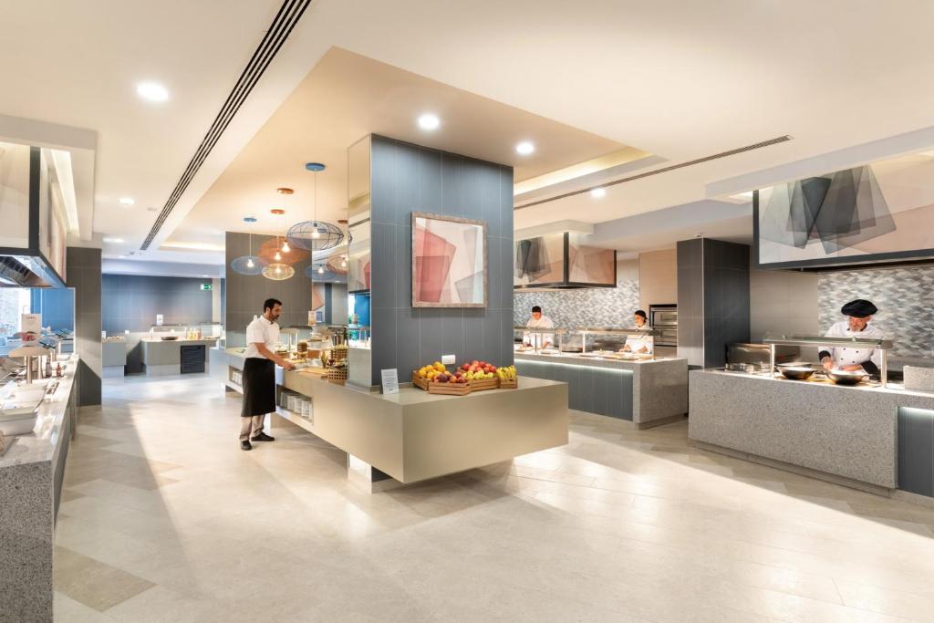 Mūsdienīga restorāna virtuve ar šefpavāriem, kas gatavo ēdienus. Skats uz eleganti iekārtotu telpu ar dažādām ēdināšanas stacijām.