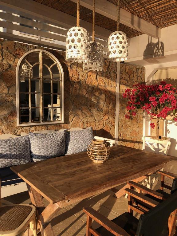 Mūsdienīgs āra terases dizains ar akmens sienu, koka galdu un krāsainām puķēm, radot relaksējošu atmosfēru. Apgaismojums no piekārtiem lampu ķermeņiem piešķir siltumu un mājīgumu.