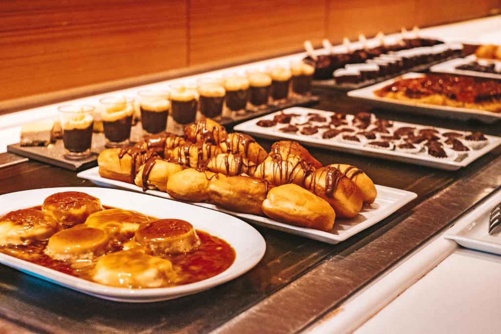 Deserts ar dažādiem saldumiem, tostarp krēma karameli, šokolādes saldējumu un kraukšķīgām kūkām, pasniegti uz baltiem šķīvjiem.