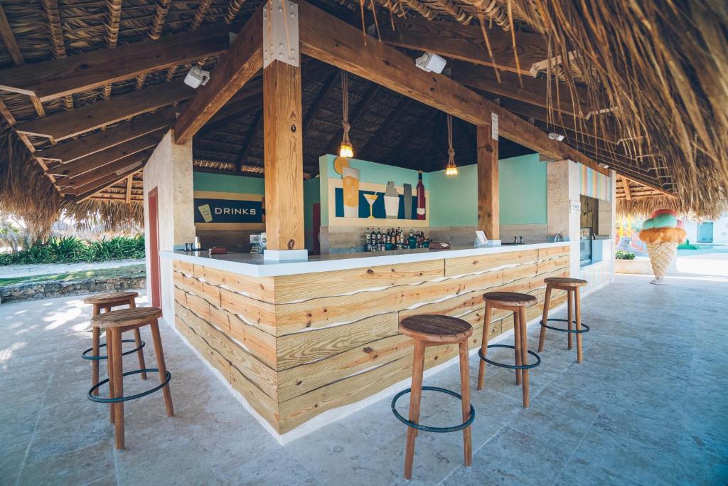 Tropu bārs ar koka letēm un augstām krēslām, atpūtas zona zem salmu jumta un krāsainu dzērienu attēliem uz sienas. Ideāla vieta relaksācijai un atsvaidzināšanai.