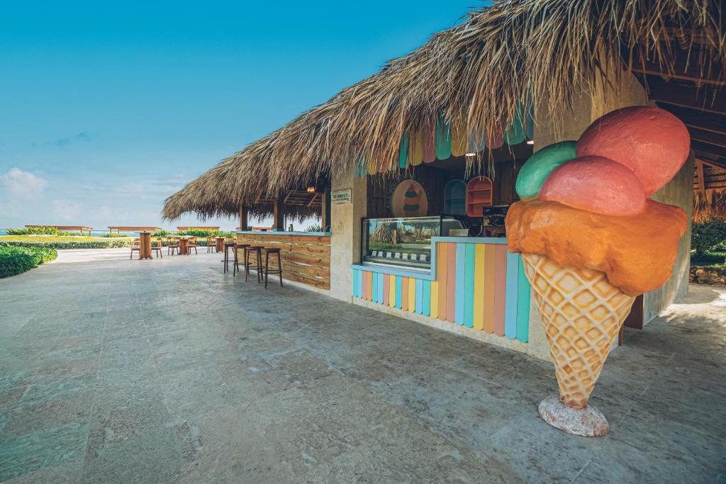 Krāsains saldējuma kiosks ar saldējuma vafeļu konusiem un dabīgā materiāla jumtu, kas atrodas pludmalē. Ideāla vieta, lai baudītu saldējumu siltā klimatā.