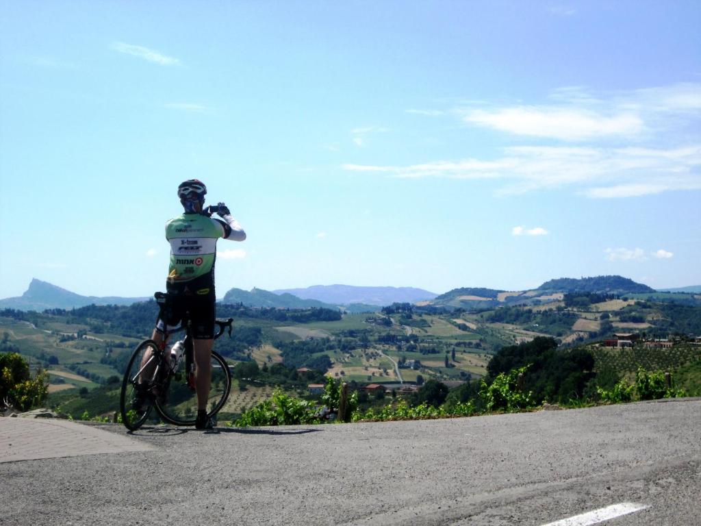 Cilvēks ar velosipēdu apbrīno skaistu ainavu no kalna, baudot dabu un mieru. Fons ir zaļi pakalni un zilas debesis.