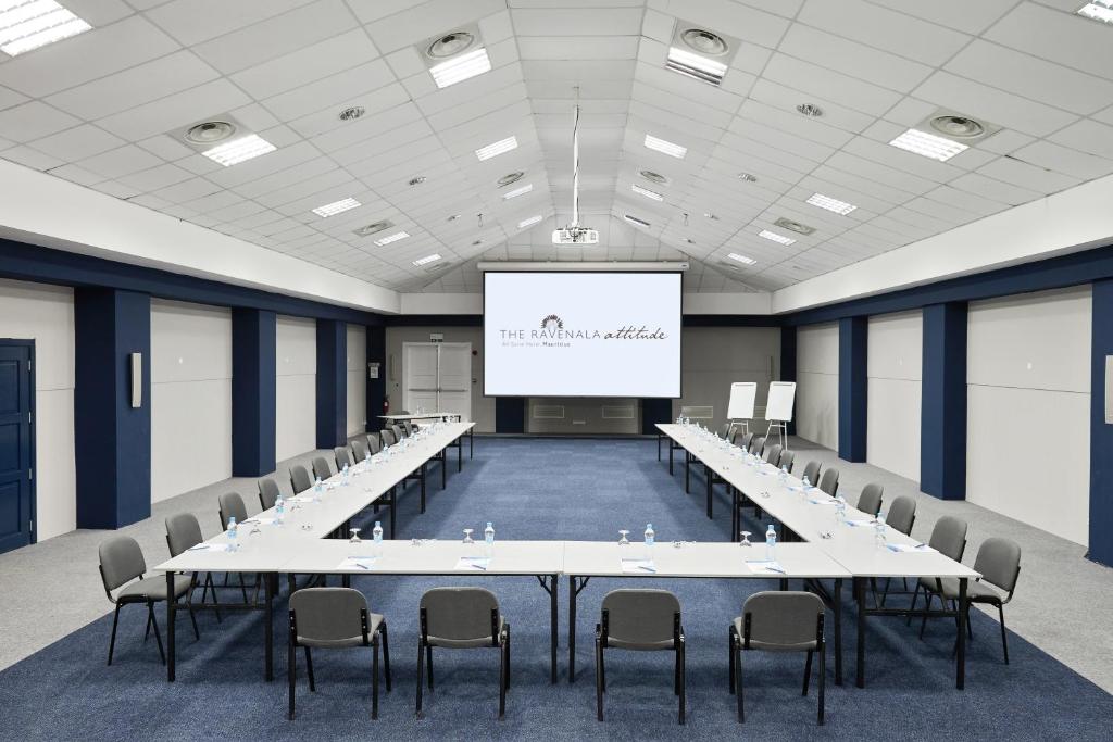 Konferences telpa ar galdu un krēsliem, uz ekrāna redzams 