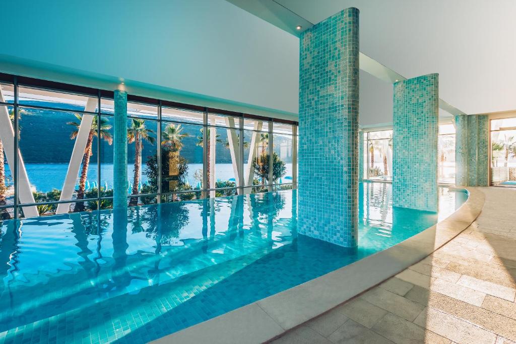 Elegantā peldbaseina ar stikla sienām un palmām, kas redzamas caur logiem, piedāvā relaksējošu atmosfēru un gleznainu skatu.