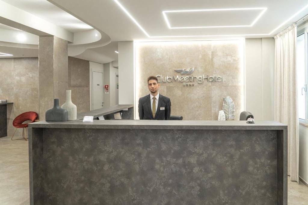 Mūsdienīgs viesnīcas reģistratūras interjers ar viesmīlīgu darbinieku pie galda un stilīgu dekori.