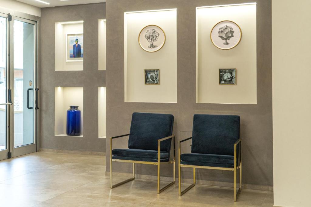 Mūsdienīgs interjers ar divām elegantiem krēsliem un mākslas darbiem uz sienas. Sienas nišās ir izstādīti dekoratīvi priekšmeti, radot stilīgu un viesmīlīgu atmosfēru.