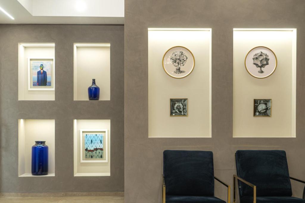 Mūsdienīgs interjers ar mākslas darbiem un zilo trauku izkārtojumu, radot elegantu atmosfēru. Sienas nišās izvietoti dažādi attēli un trauki, papildinot telpas dizainu.