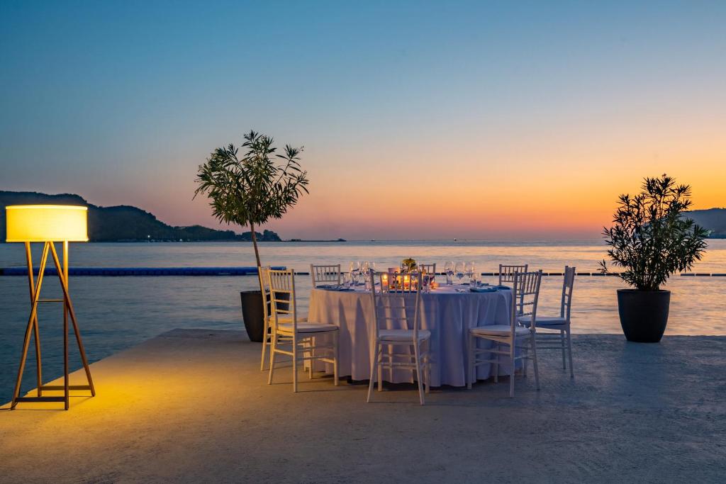 Romantiska vakariņas pie jūras ar galdu, kas klāts ar baltu galdautu, un skaistu saulrietu fona. Apgaismojums un zaļumi pie galda rada burvīgu atmosfēru.