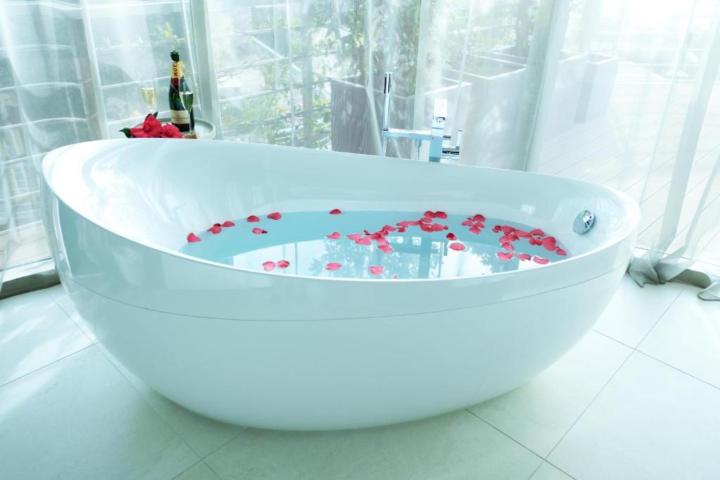 Luksusa vannistaba ar rozā ziedlapiņām ūdenī un šampanieša pudeli, kas radījuši relaksējošu atmosfēru.