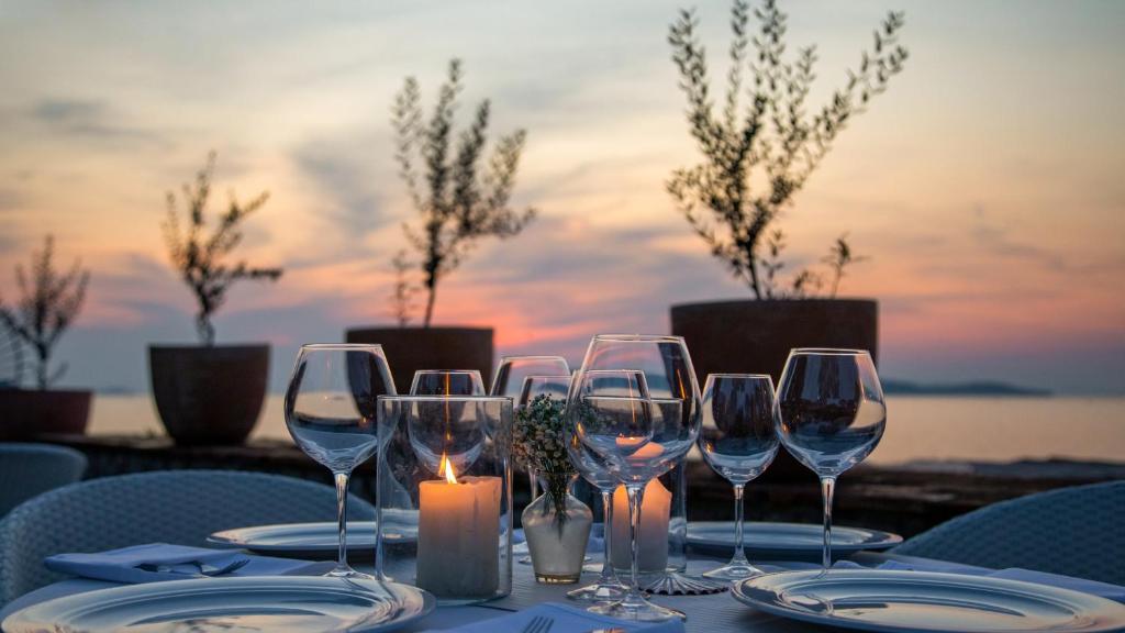 Romantiska vakariņas ar galdu, kas klāts pie ūdens, sveces un glāzes saulrieta gaismā.