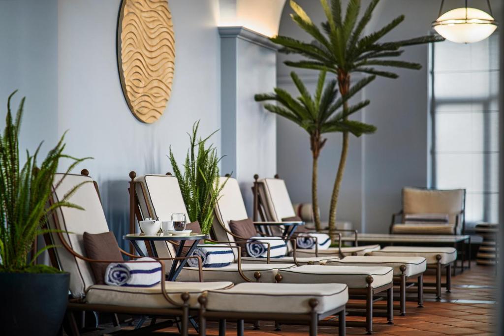 Mūsdienīgs atpūtas stūris ar ērtiem saulessargiem, zaļām augu kompozīcijām un dekoratīvu sienas mākslu, radot relaksējošu atmosfēru.