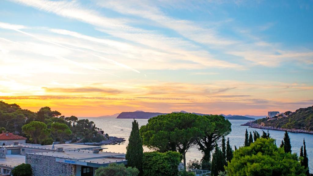 Krāšņa jūras ainava ar saulrietu, kurā redzami zaļi koki un kalni fona, radot mierīgu un gleznainu atmosfēru.