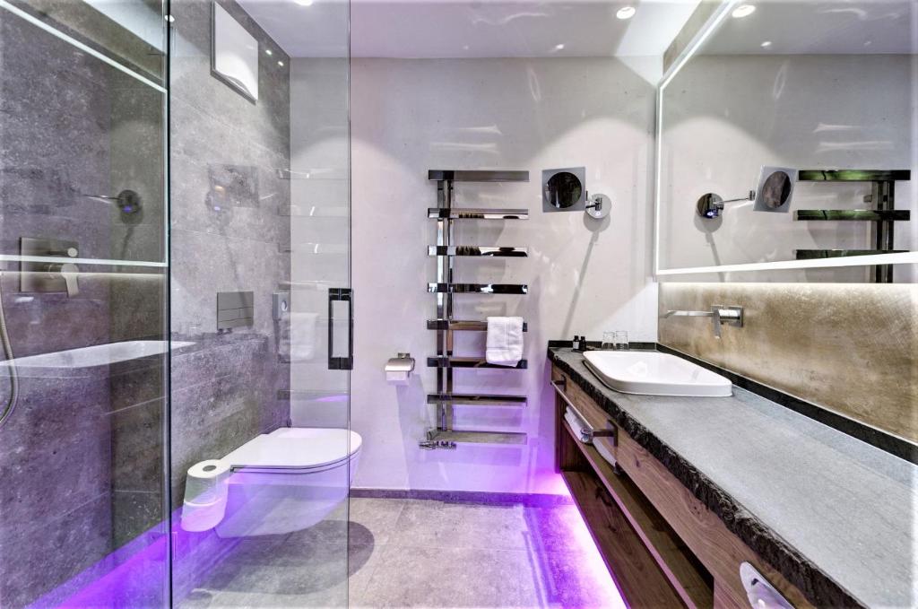 Mūsdienīgs vannas istabas interjers ar stikla durvīm, pelēkām akmens sienām un gaišu apgaismojumu. Labi organizēta telpa ar elegantu izlietni un modernu tualeti.