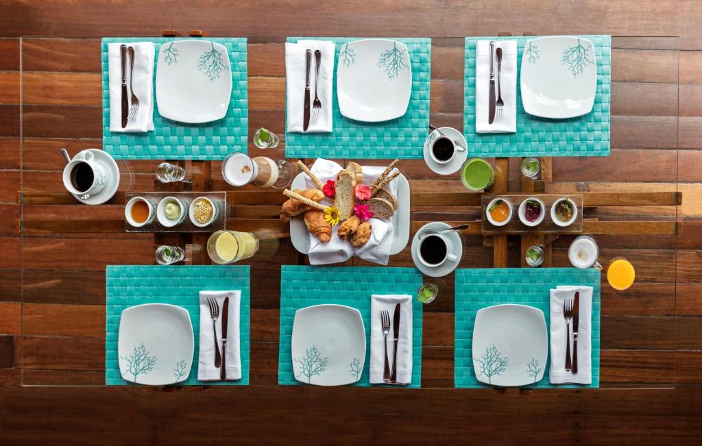 Eleganti izklāta brokastu galda kompozīcija ar zaļu paklājiņu, baltām šķīvjiem un gardumiem, piemēram, maizītēm un augļu sulām. Galda centrā atrodas dažādas mērces un dzērieni.