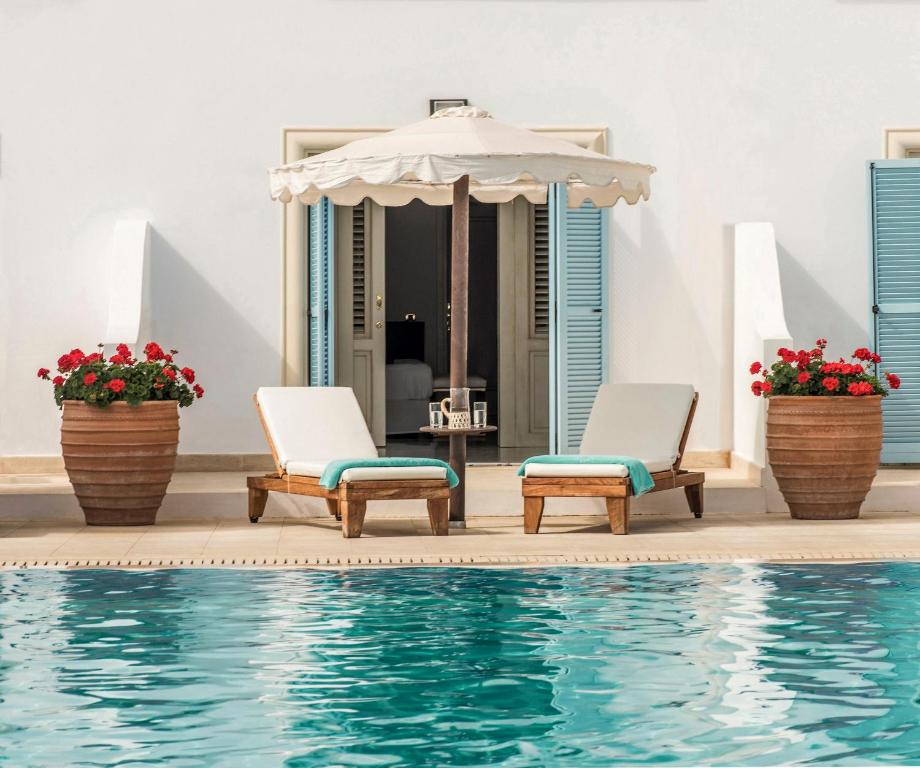 Atpūtas zona pie baseina ar diviem saulessargiem un ziedu podiem, izsmeļot mierīgu un relaksējošu atmosfēru. Dabas krāsas un stilīga arhitektūra rada ideālu vietu atpūtai.