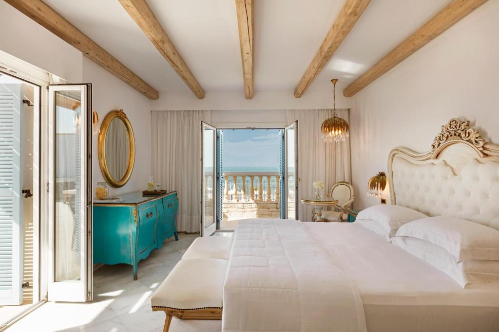 Mūsdienīgs guļamistabas interjers ar gaisīgiem koka griestiem un skatu uz jūru. Telpā ir eleganta gulta, zila komoda un lieli logi, kas nodrošina daudz dabiskās gaismas.