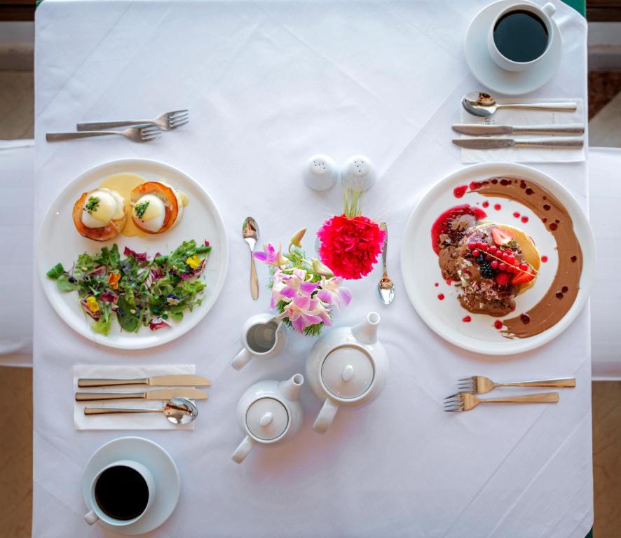 Elegants brokastu galds ar pošu ziedu kompozīciju, diviem šķīvjiem, kas satur olu benediktu un saldējuma desertu, kā arī kafiju un tēju.