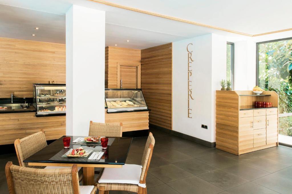 Mūsdienīga kafejnīca ar koka apdari, kurā redzama galda uzstādīšana un izstādes vitrīnas desertiem. Gaisīga telpa ar dabīgu apgaismojumu un augu akcentiem.