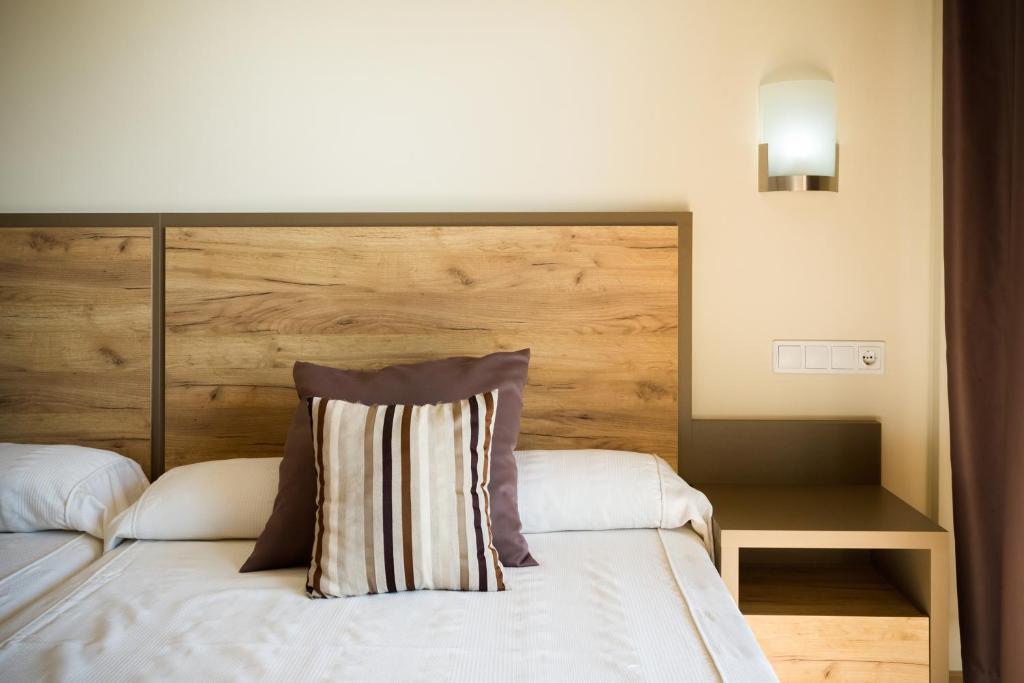 Mūsdienīgs guļamistabas interjers ar koka gultas galvu un strīpainu spilvenu. Sienas lampiņa un naktsgaldiņš pie gultas papildina kopējo dizainu.