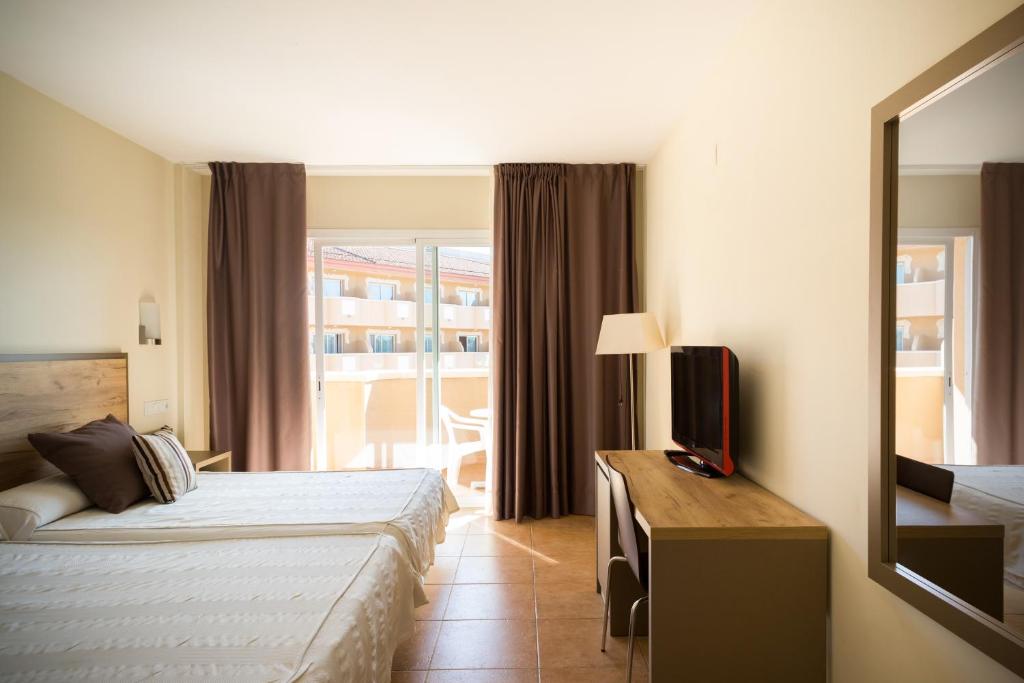 Gaiša viesnīcas numuriņa iekārtojums ar divām gultām, televizoru un rakstāmgaldu, kā arī logu ar skatu uz terasi. Drapējumi rada mājīgu atmosfēru.