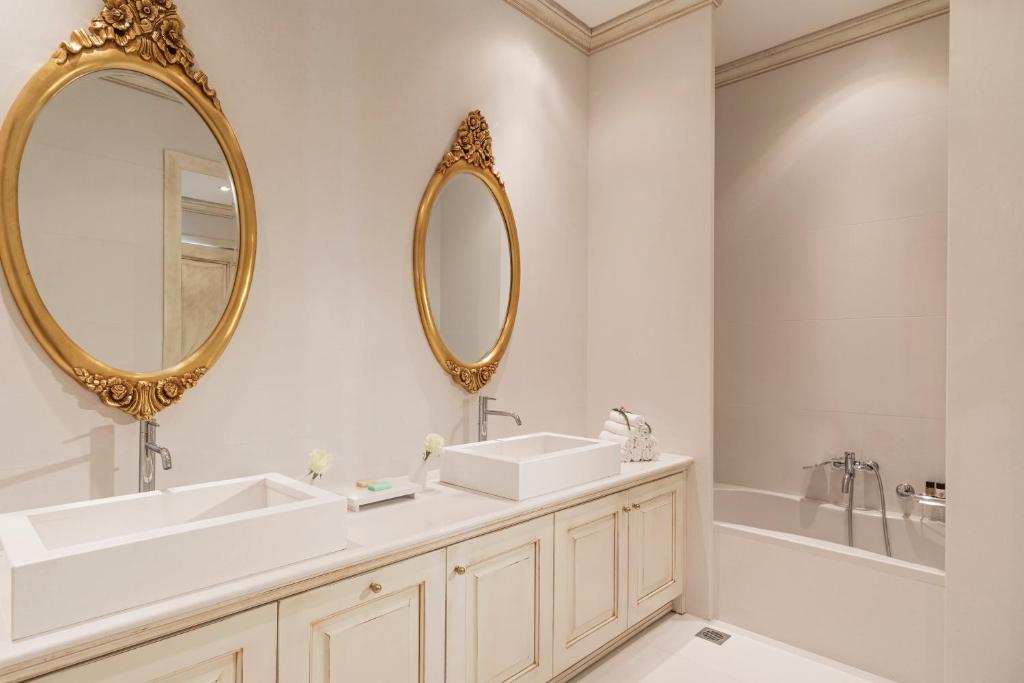 Elegants vannas istabas interjers ar divām apļveida spogulēm ar zelta rāmjiem un mūsdienīgām izlietnēm uz koka skapīša. Vannas istabā ir gaišas krāsas un minimālistisks dizains.