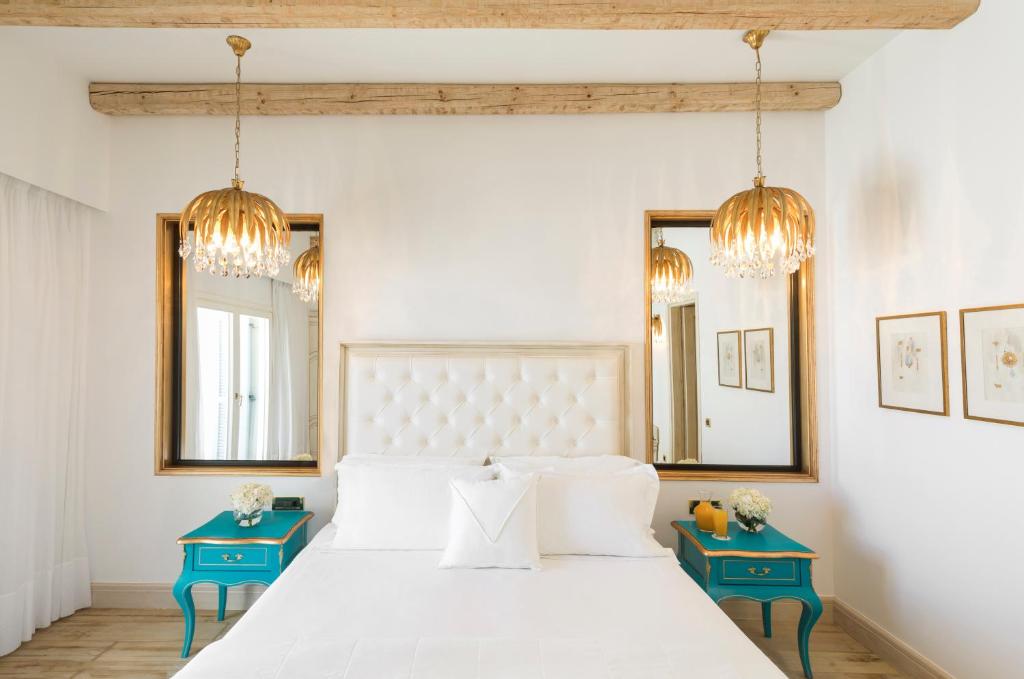 Mūsdienīgs guļamistabas interjers ar spilgtu zilo naktsgaldiņu un elegantu zelta lampu, kas piešķir siltumu un gaismu. Sienas rotā spoguļi un mākslas darbi, radot stilīgu un komfortablu atmosfēru.