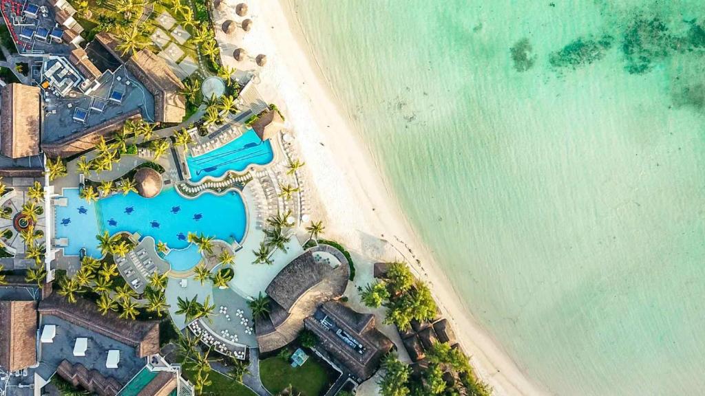 Tūrisma kūrorts ar baseinu un pludmali, ko ieskauj palmas, gleznainā ainavā. Skaists skats uz kristāldzidru ūdeni un smilšu krastu.