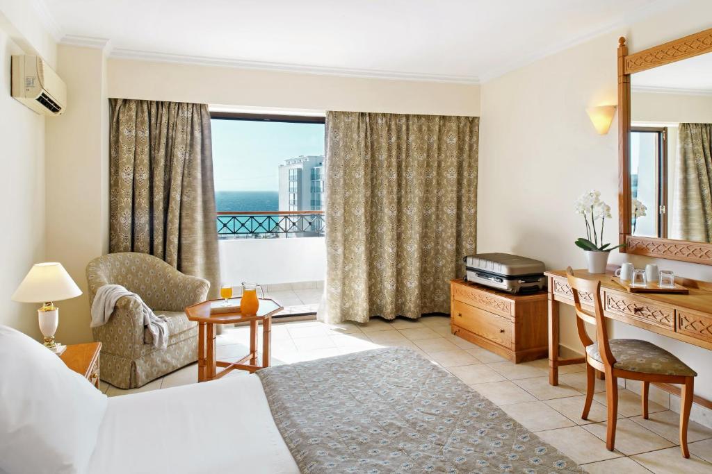 Mūsdienīgs viesnīcas numurs ar skatu uz jūru, iekārtots ar ērtu krēslu, mazu galdiņu un dekoratīvām aizkarām. Numurā ir gaismas avots un koka mēbeles.