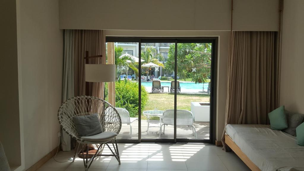 Mūsdienīgs numurs ar skatu uz baseinu, kurā ir ērta balta krēsla un gultas. Daba un atpūtas zonas rada relaksējošu atmosfēru.