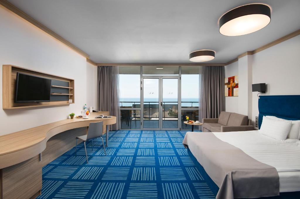 Moderns viesnīcas numurs ar skatu uz jūru, iekārtots ar ērtu gultu, dīvānu un darba vietu. Telpā ir lieli logi, kas ļauj ienākt dabiskai gaismai, un ir pieejama modernā televizora un galda kombinācija.