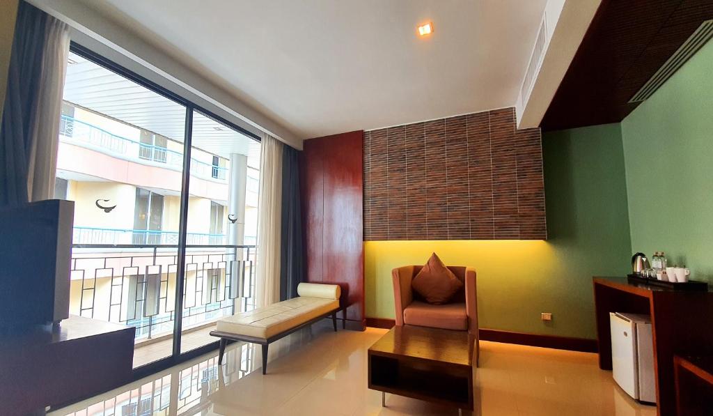 Mūsdienīgs viesnīcas numurs ar plašu logu, kas nodrošina dabiska apgaismojuma plūsmu, un elegantu interjeru, kurā ir dīvāns, atpūtas krēsls un koka galdiņš.